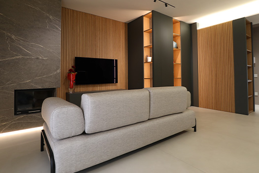 Divano in zona giorno con parete attrezzata in legno con camino e tv a scomparsa